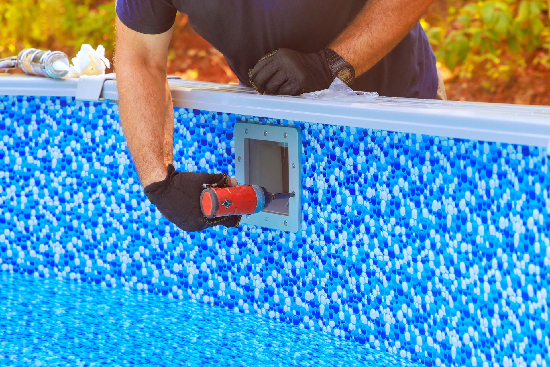 Worker performing maintenance on backyard swimming pool in sunny outdoor setting